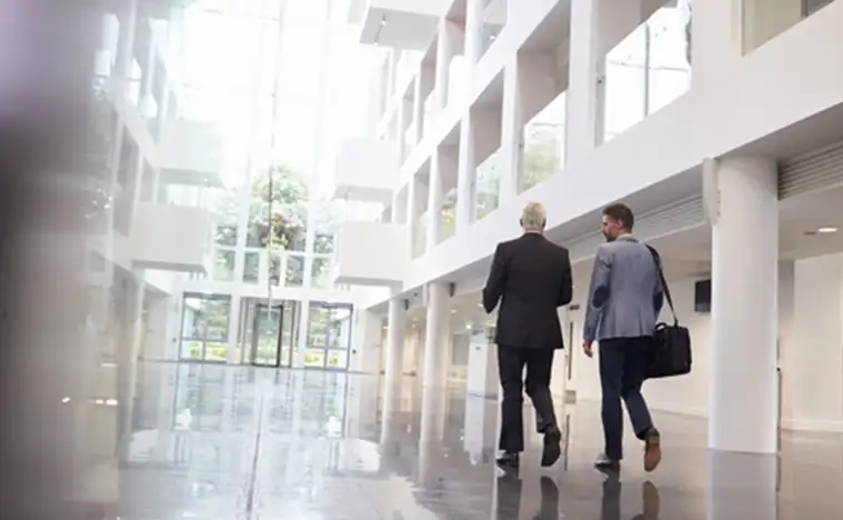 Rear View Of Businessmen Walking Through Office Lobby
