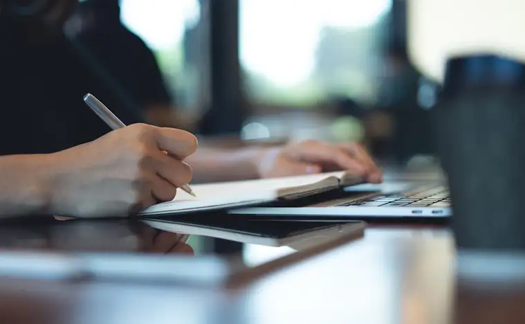 Taking notes in a notepad while looking over reports.